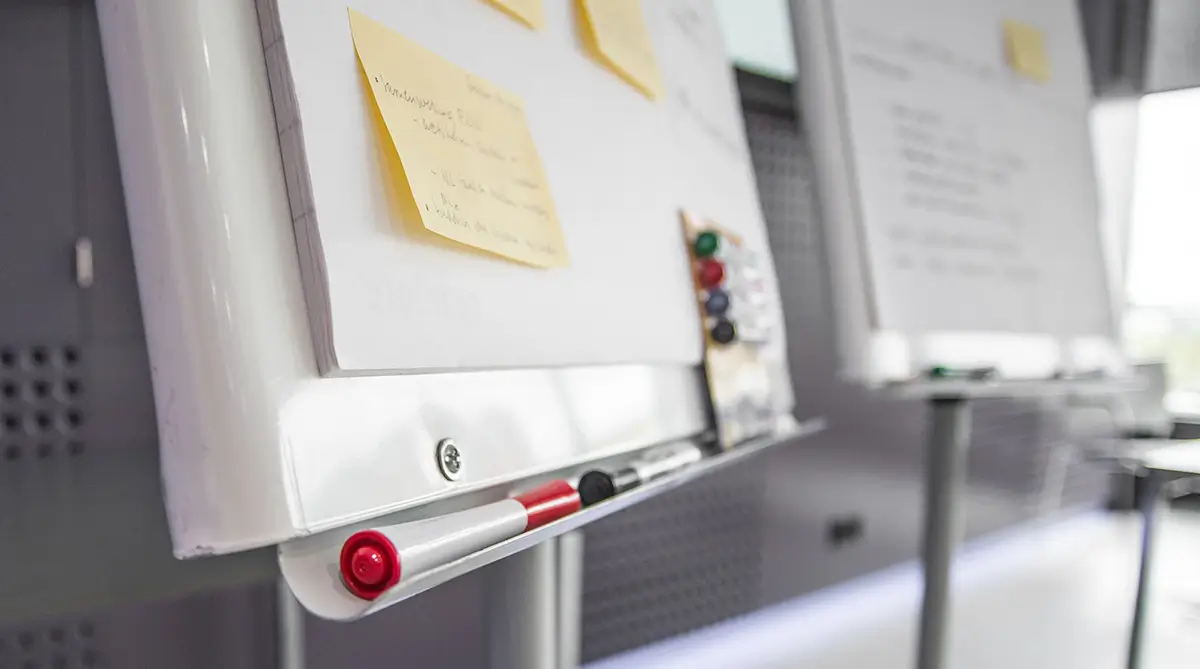 A whiteboard with post-it notes stuck to it, and markers sitting on the ledge.