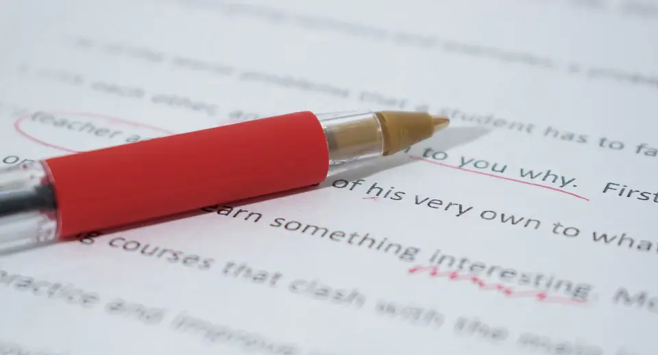 A red pen lies on top of a manuscript, with edits having been made in red.
